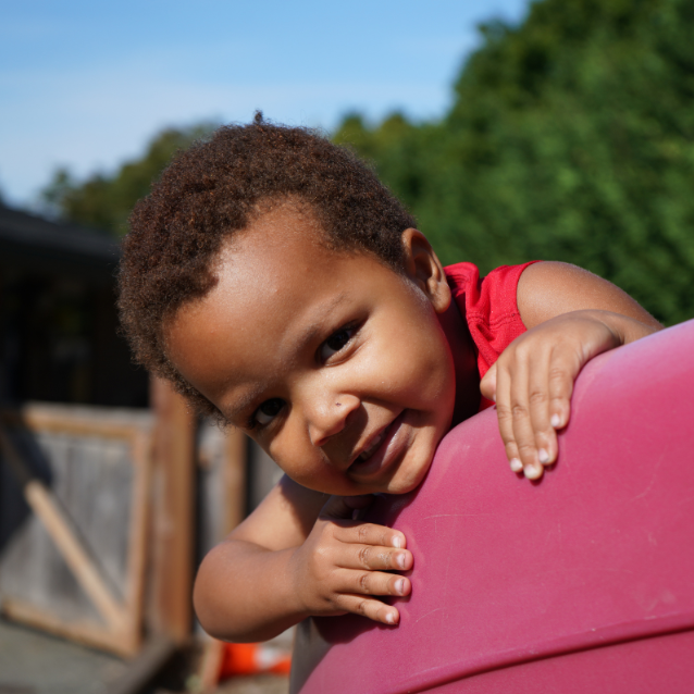 Kid smiling over slide A young kid leans over a red slide and smiles